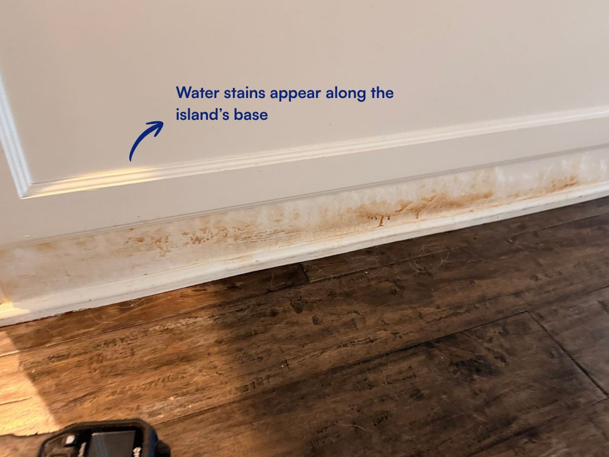 Water stains along the base of the kitchen island, above the wood flooring.
